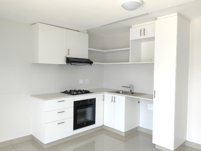 Modern, clean-lined kitchen featuring white cabinetry, stone countertops, integrated gas hob, oven, and extractor fan, with neutral tiled flooring.