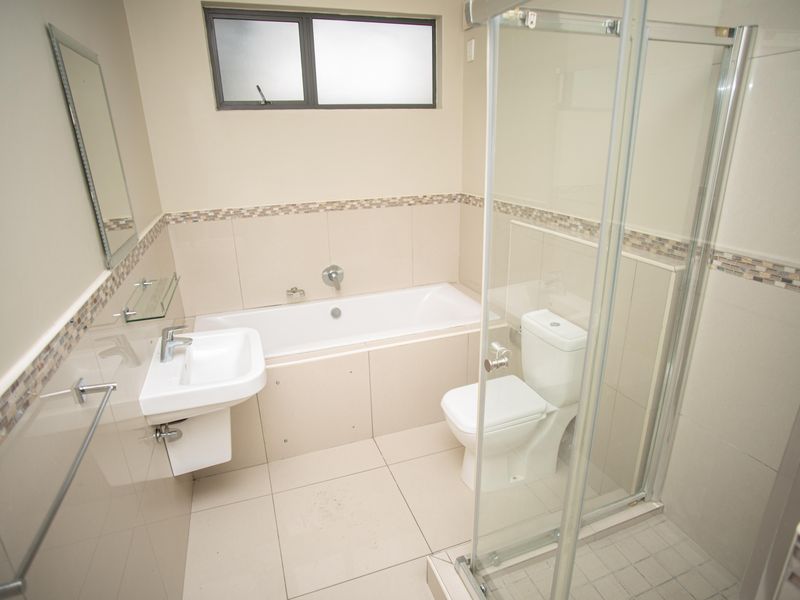 A clean, modern bathroom featuring a bathtub, separate shower enclosure, wall-mounted basin, and toilet with neutral tiled finishes.