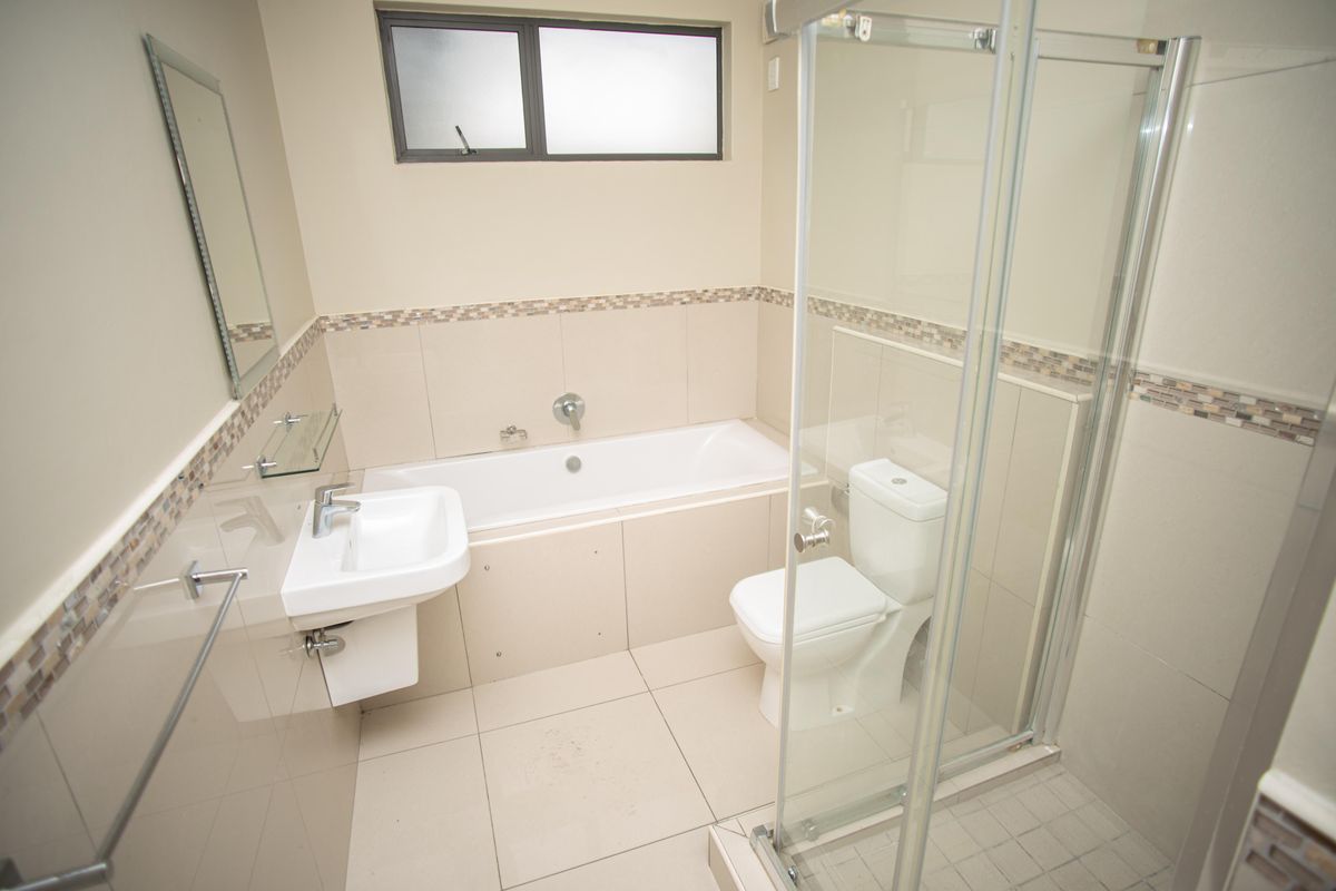 A clean, modern bathroom featuring a bathtub, separate shower enclosure, wall-mounted basin, and toilet with neutral tiled finishes.