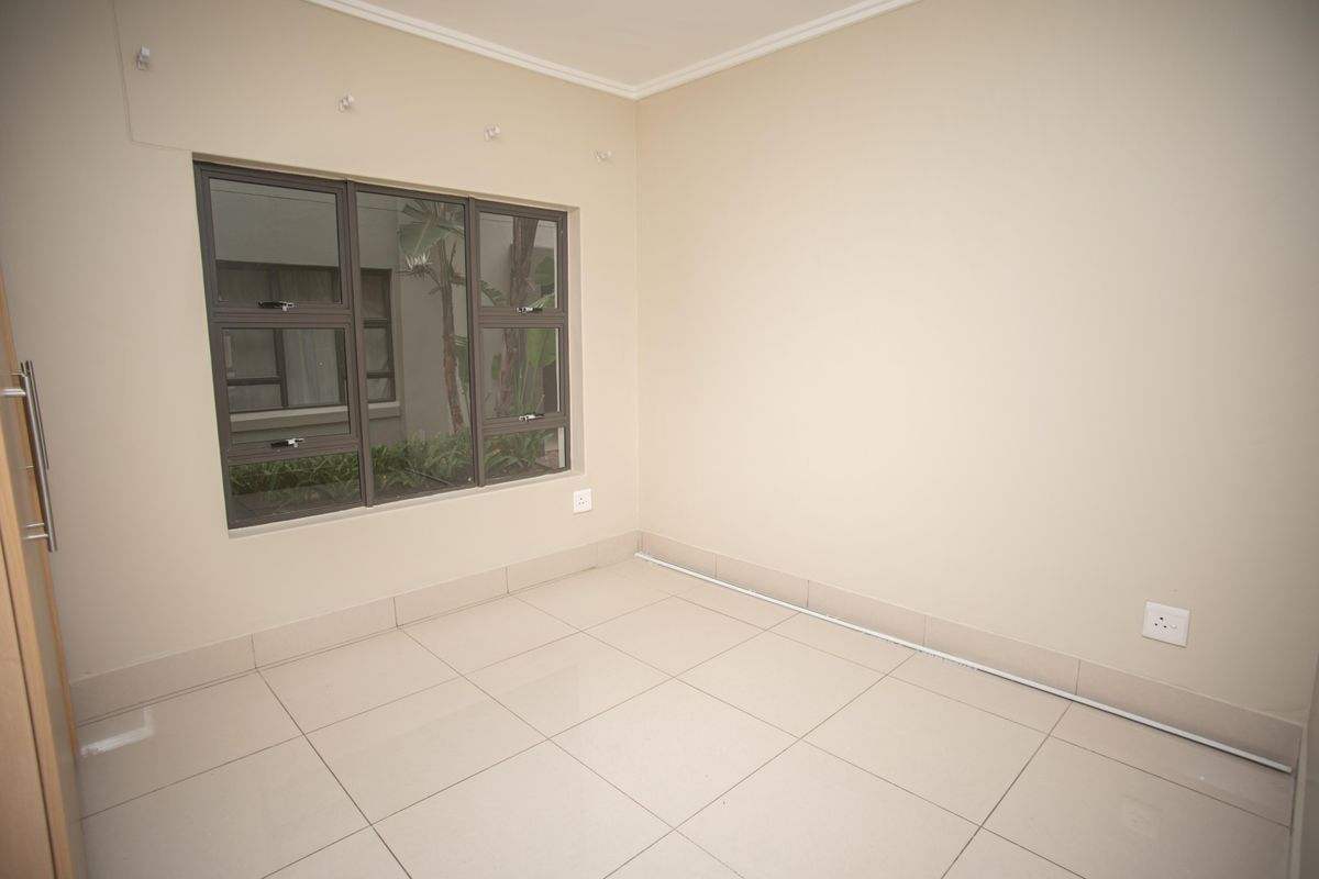 An empty bedroom featuring neutral tiled flooring, a built-in cupboard, and an aluminium-framed window overlooking an exterior courtyard.