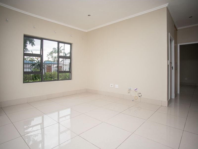 A bright, empty living room featuring neutral walls, polished tiled flooring, and aluminium-framed windows, offering a clean and versatile space.
