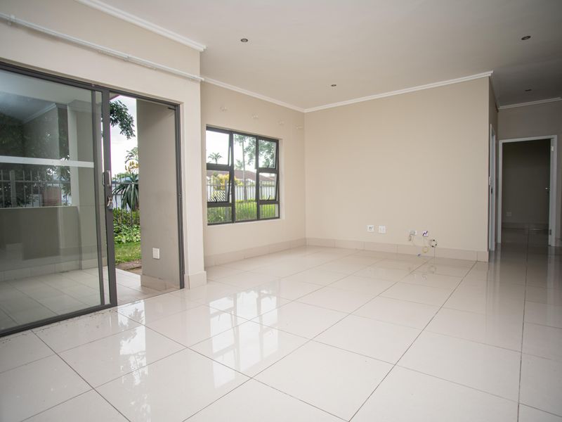 A bright, empty living room featuring polished tiled floors, recessed lighting, and a sliding glass door providing access to the outdoor area.