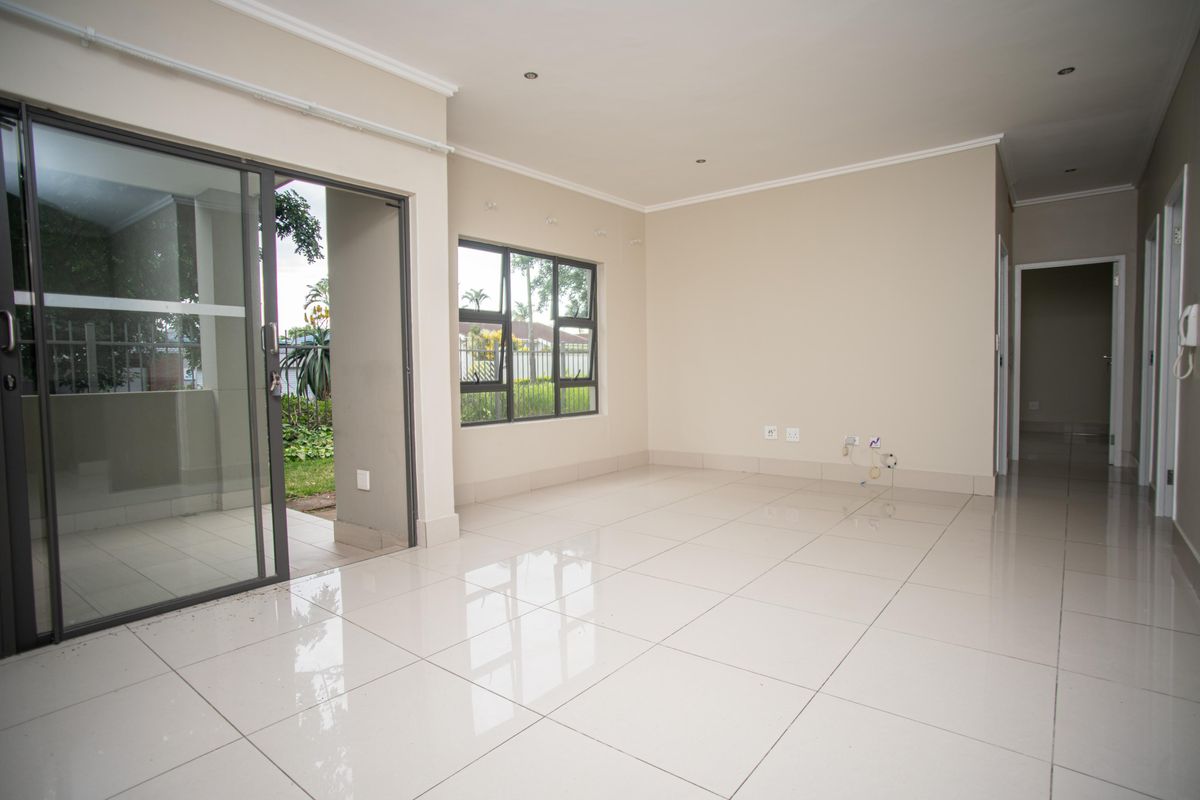 A bright, empty living room featuring polished tiled floors, recessed lighting, and a sliding glass door providing access to the outdoor area.