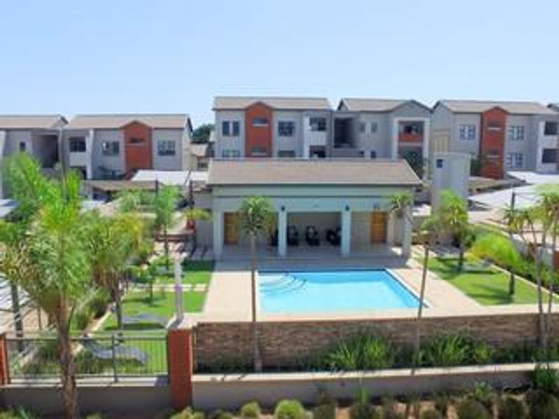 An elevated view of a communal swimming pool area featuring a clubhouse, stone-clad retaining wall, and landscaped garden within an apartment complex.