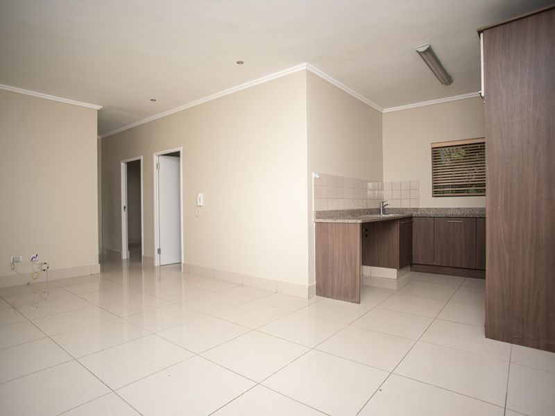 An open-plan living and kitchen area featuring neutral tiled flooring, modern dark wood cabinetry, granite countertops, and a functional layout.