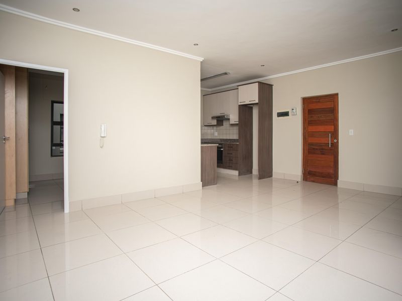 Spacious open-plan living area featuring neutral tiled flooring, recessed lighting, and an integrated kitchen with modern cabinetry and built-in appliances.