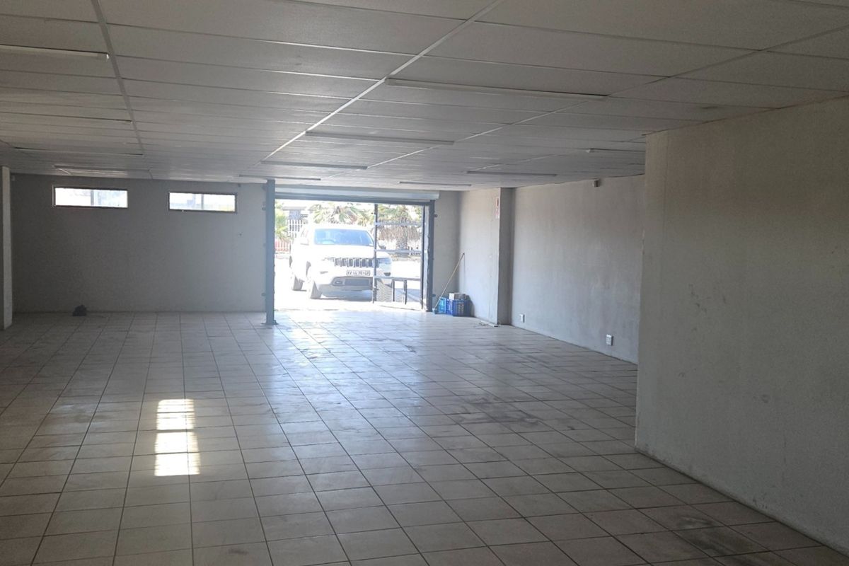 A spacious, empty open-plan commercial area featuring tiled flooring, a suspended ceiling, and natural light access through a secure entrance.