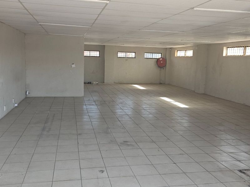 A spacious, vacant open-plan commercial unit featuring ceramic tiled flooring, a suspended ceiling, and security-barred windows, suitable for various business applications.