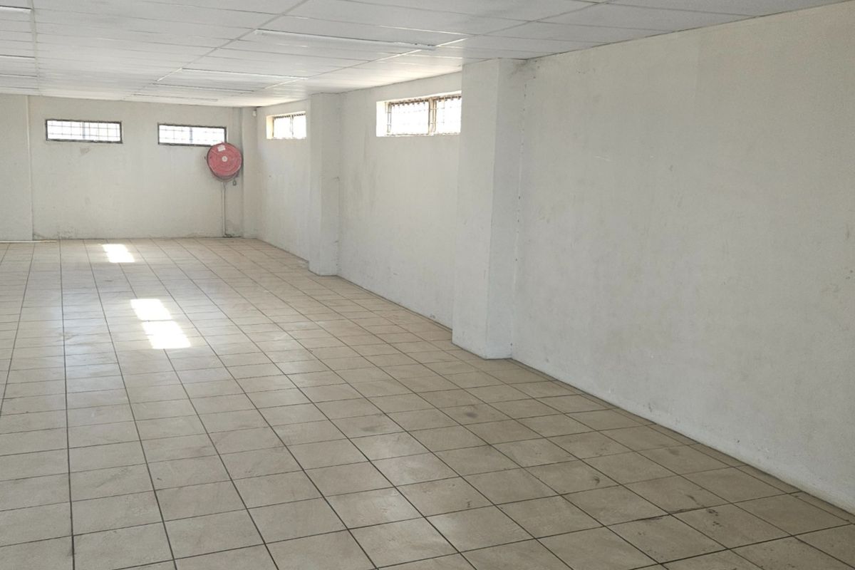 A large, vacant open-plan commercial space featuring tiled flooring, a suspended ceiling, and a wall-mounted fire hose reel.