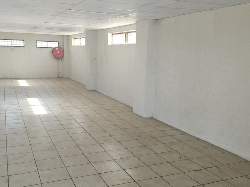 A large, vacant open-plan commercial space featuring tiled flooring, a suspended ceiling, and a wall-mounted fire hose reel.