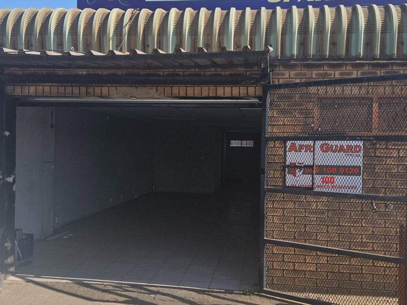 Commercial storefront entrance featuring a brick facade, metal security gate, and corrugated metal awning, providing access to an open-plan interior space.