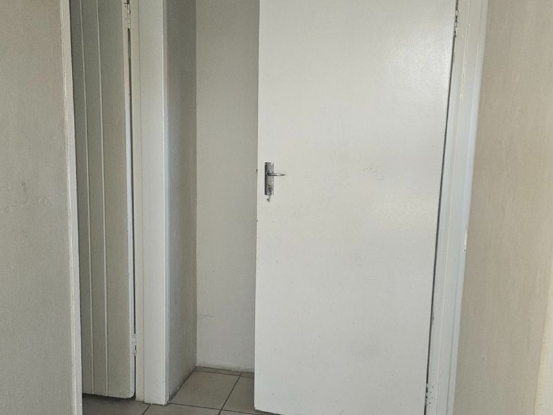 A simple interior hallway featuring tiled flooring and multiple internal doors, showing signs of wear on the wall surfaces.