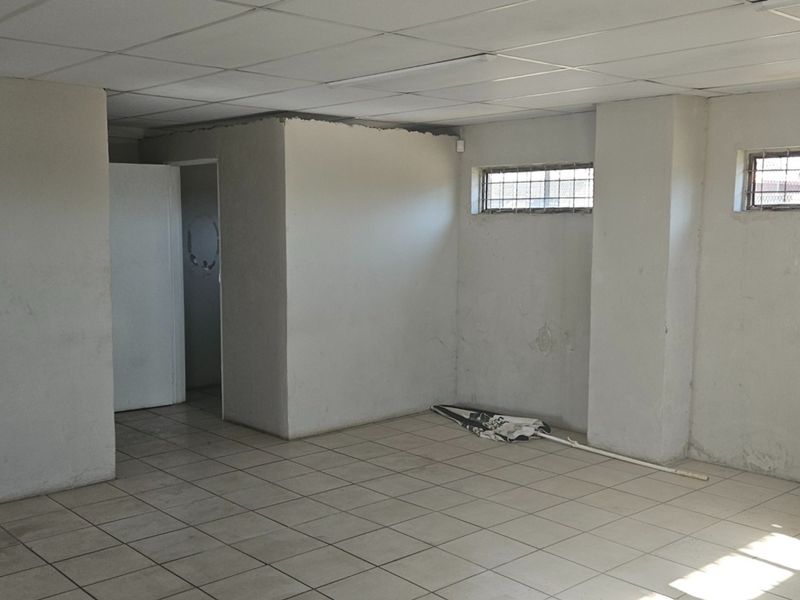 An empty, open-plan office space featuring ceramic floor tiles, a suspended ceiling, and windows fitted with security bars.