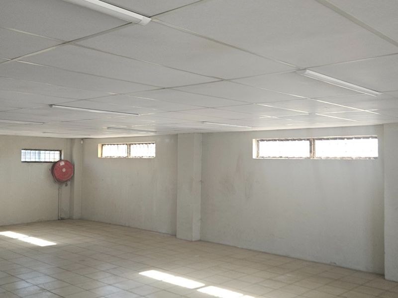 An open-plan office space featuring tiled flooring, a suspended ceiling with integrated lighting, and security-barred windows.