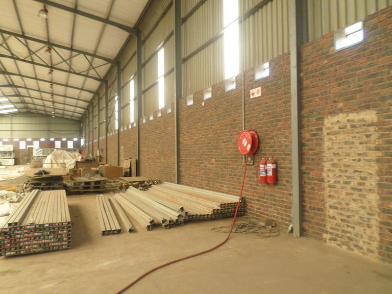 Spacious industrial warehouse unit featuring high ceilings with exposed steel trusses, face brick walls, concrete flooring, and integrated fire safety equipment.
