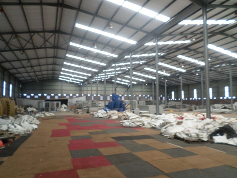 Large industrial warehouse space featuring a steel portal frame structure, translucent roof panels for natural light, and high bay lighting.