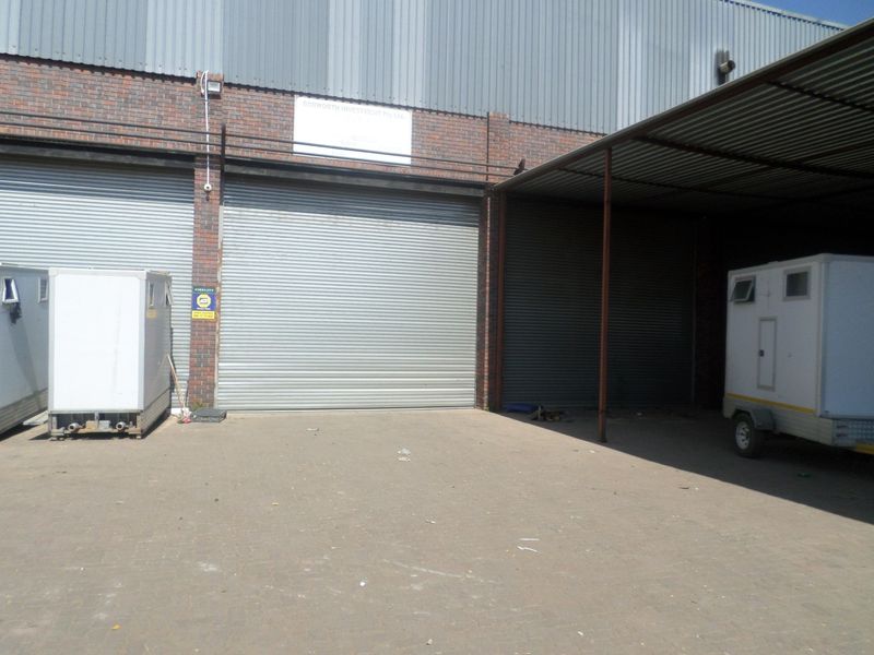 Industrial property exterior featuring multiple roller shutter doors, a covered loading area, and a paved yard space.