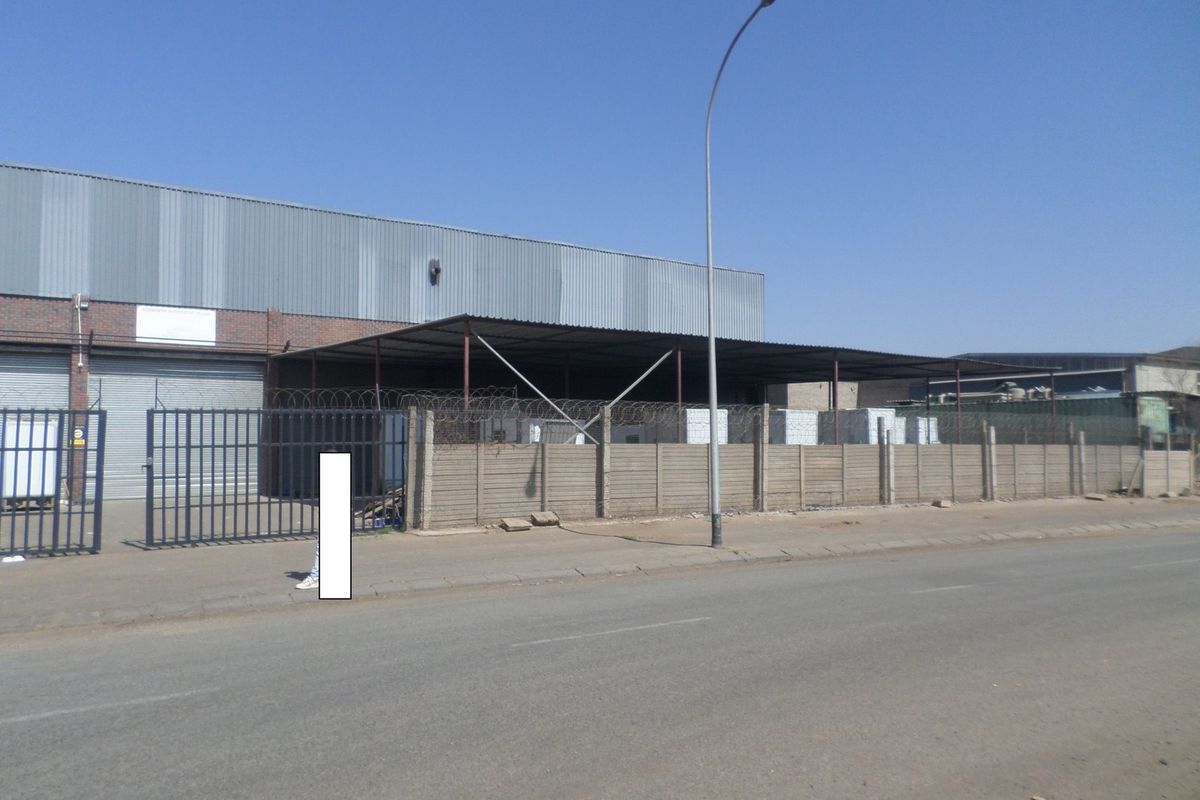 Industrial property exterior featuring corrugated metal cladding, a roller shutter door, and secure perimeter fencing with razor wire.