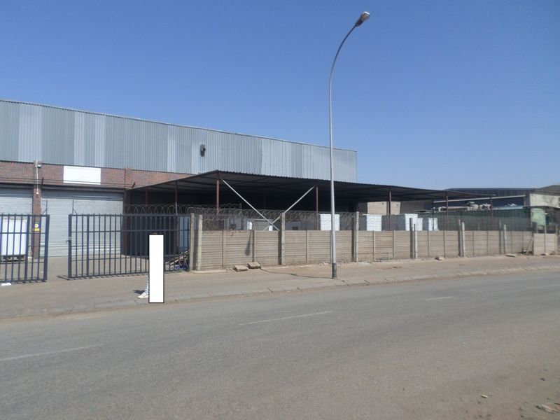 Industrial property exterior featuring corrugated metal cladding, a roller shutter door, and secure perimeter fencing with razor wire.