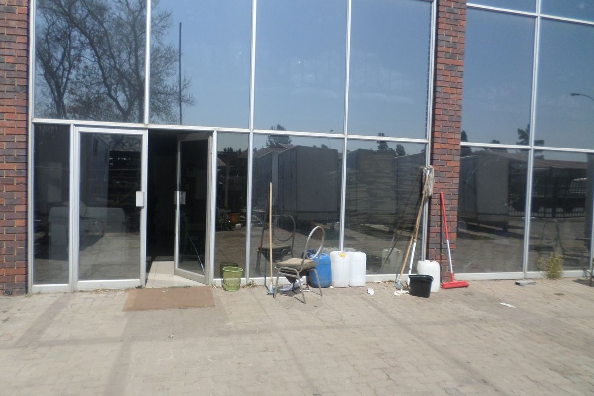 Front exterior view of an industrial building featuring a brick facade and large aluminium-framed glass windows with a paved entrance area.