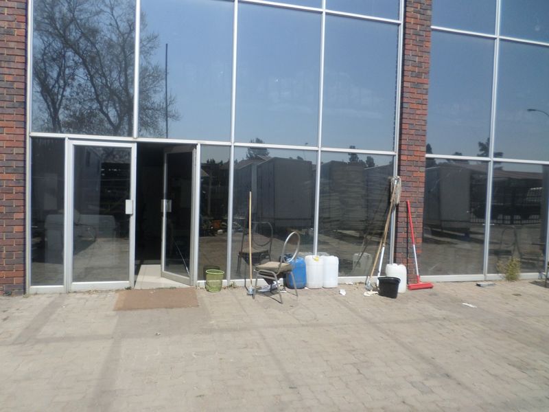 Front exterior view of an industrial building featuring a brick facade and large aluminium-framed glass windows with a paved entrance area.