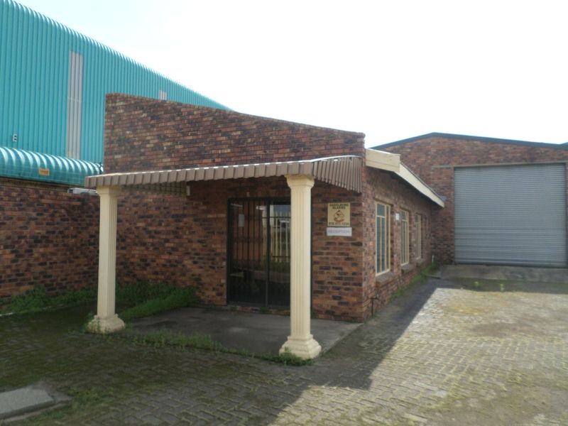 Industrial property exterior featuring a face brick facade, covered entrance porch with decorative columns, and a large roller shutter door for vehicle access.