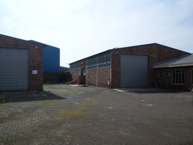 Industrial yard area featuring multiple brick warehouse buildings with large roller shutter doors and paved access space.