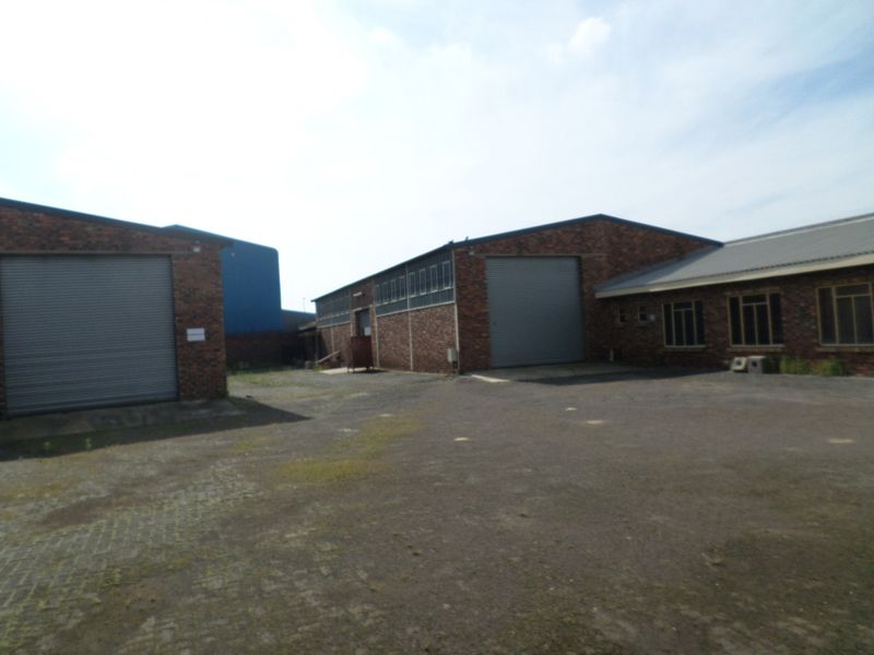 Exterior view of an industrial property featuring multiple roller shutter doors, brick construction, and a large paved yard area.