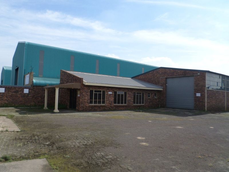 Industrial property featuring a brick facade, metal roller shutter door, and a large warehouse structure with a paved driveway and covered entrance.