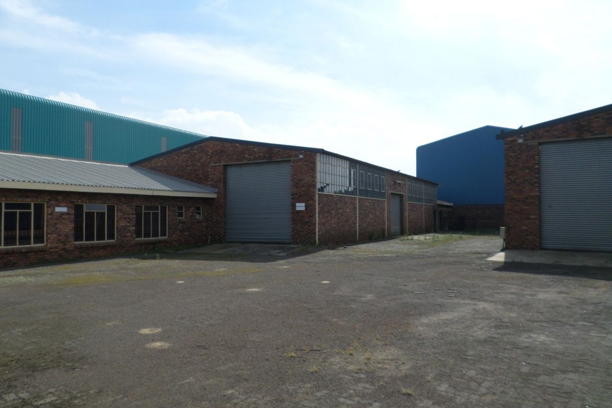 Exterior view of an industrial property featuring multiple warehouse buildings with roller shutter doors, brick facades, and a large paved yard area.