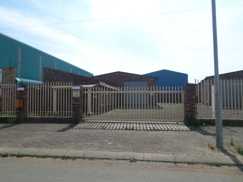 Front view of an industrial property featuring a brick facade, secure steel palisade fencing, and a roller shutter door access point.