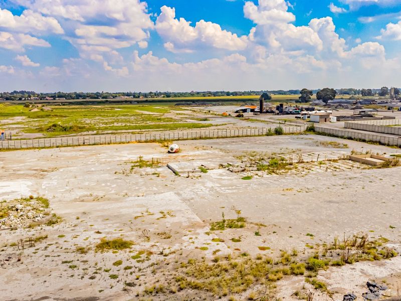 Aerial view of a large industrial plot featuring a concrete slab foundation, perimeter fencing, and surrounding open land.