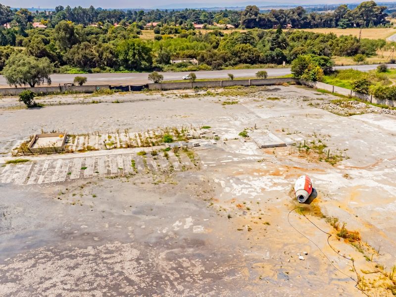 Aerial view of a large industrial yard featuring extensive concrete surfacing, perimeter walling, and remnants of former structural foundations.
