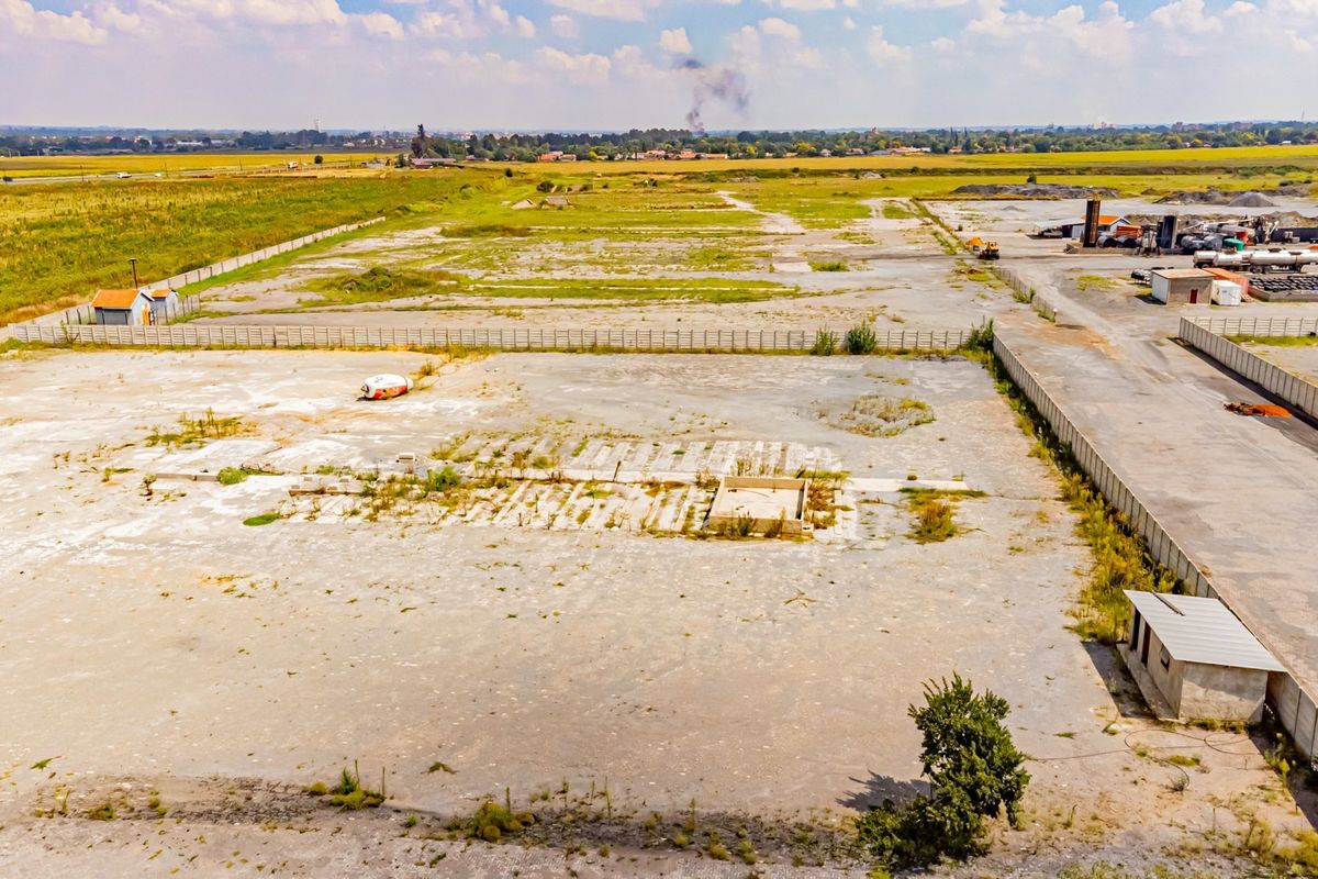 Aerial view of a large industrial site featuring extensive concrete hardstand, perimeter fencing, and a small utility structure, suitable for redevelopment or storage.