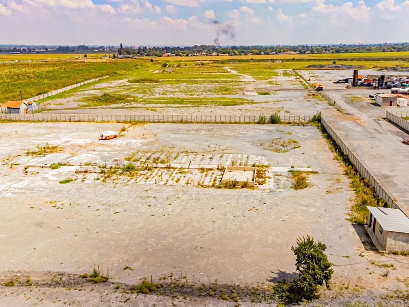Aerial view of a large industrial site featuring extensive concrete hardstand, perimeter fencing, and a small utility structure, suitable for redevelopment or storage.