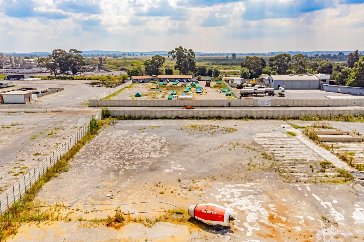 Aerial view of a large industrial yard featuring extensive paved areas, perimeter fencing, and concrete boundary walls in an established industrial zone.