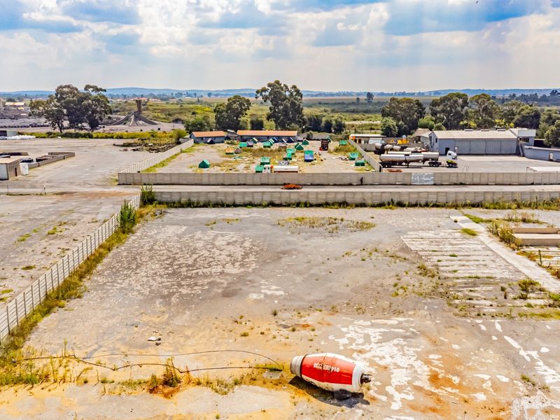 Aerial view of a large industrial yard featuring extensive paved areas, perimeter fencing, and concrete boundary walls in an established industrial zone.