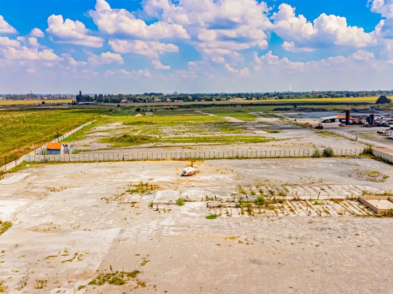 Aerial view of a large industrial plot featuring a concrete slab foundation, perimeter fencing, and surrounding open land.