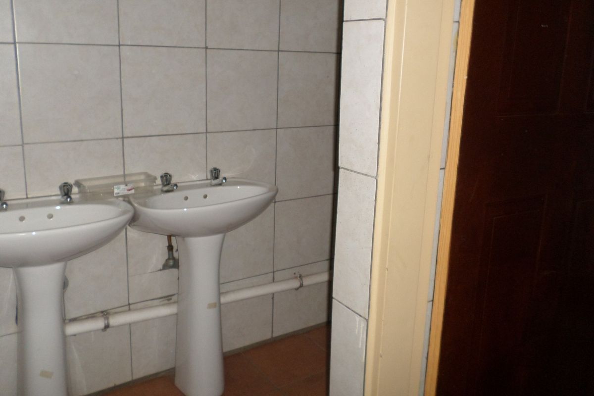 A functional bathroom space featuring dual pedestal wash basins and tiled walls, currently in need of cosmetic updates and plumbing concealment.
