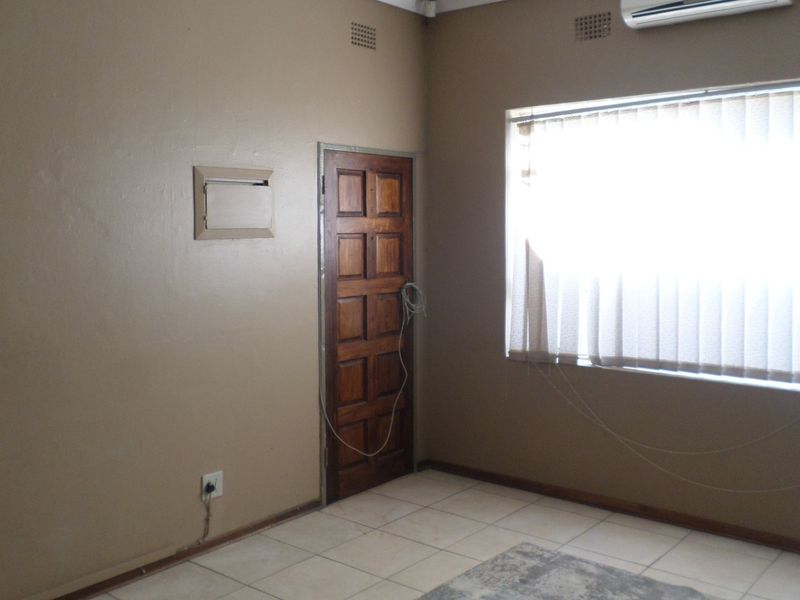 A vacant office space featuring tiled flooring, a wall-mounted air conditioning unit, and a large window with vertical blinds.