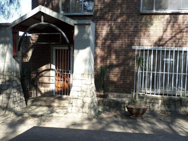 Front entrance of an office building featuring a brick facade, stone-clad pillars, and security bars on windows.