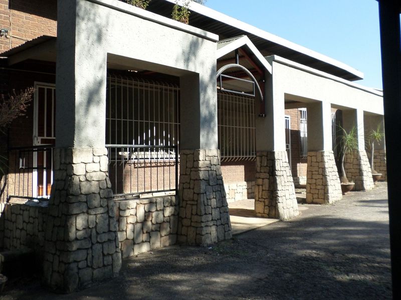 Front exterior view of an office building featuring stone-clad pillars, security bars on windows, and a covered walkway entrance.