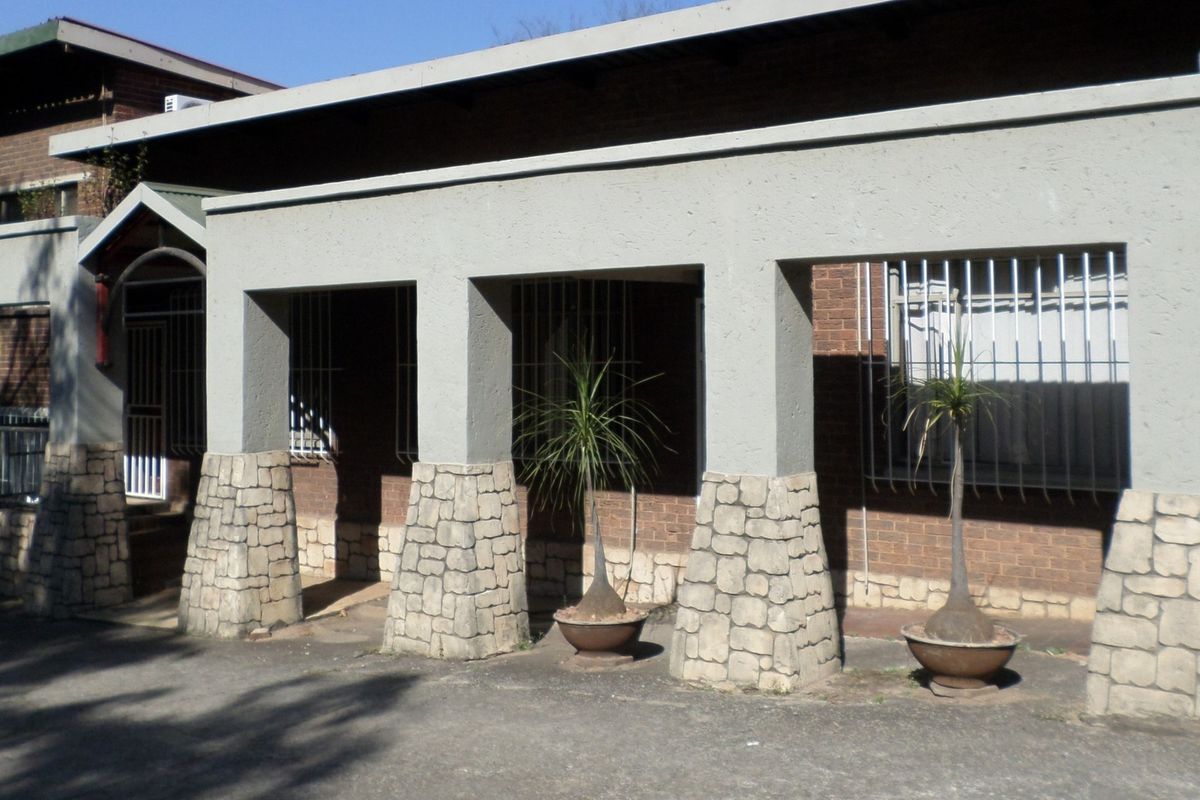 Front exterior view of an office building featuring a covered entrance with stone-clad pillars and security bars on the windows.
