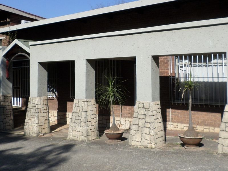 Front exterior view of an office building featuring a covered entrance with stone-clad pillars and security bars on the windows.
