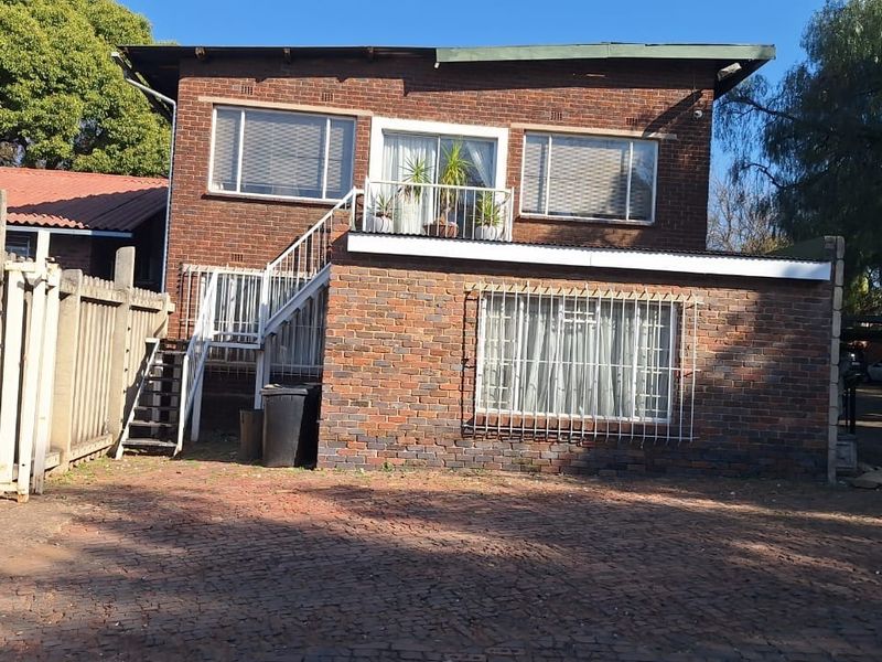 Front view of a two-story brick office building featuring an external metal staircase, balcony, and paved driveway area.