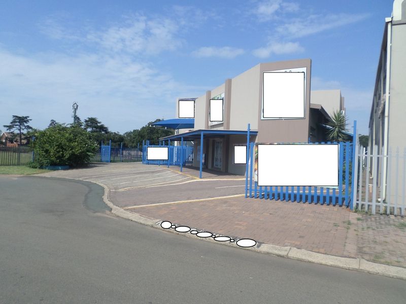 Front exterior view of a commercial property featuring a paved driveway, steel palisade fencing, and a covered entrance canopy with multiple signage boards.