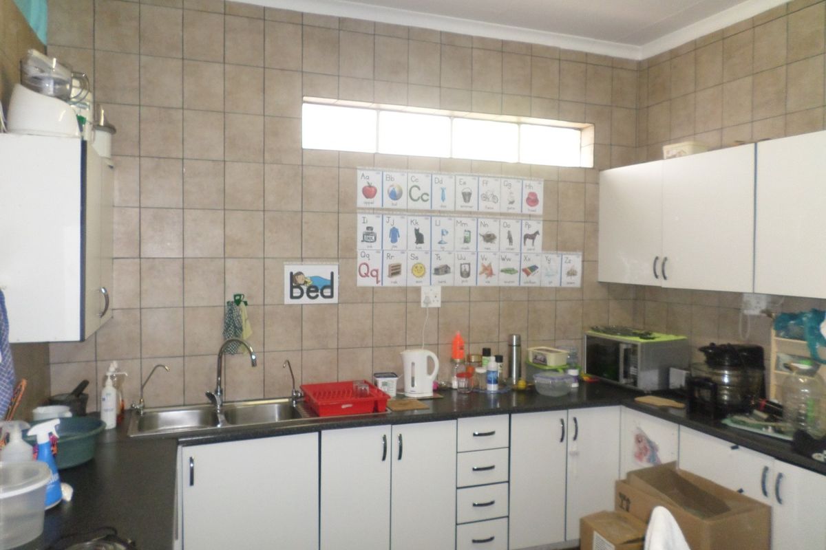 A functional kitchen featuring white cabinetry, dark laminate countertops, a double basin sink, and tiled splashback walls with a high-level window.