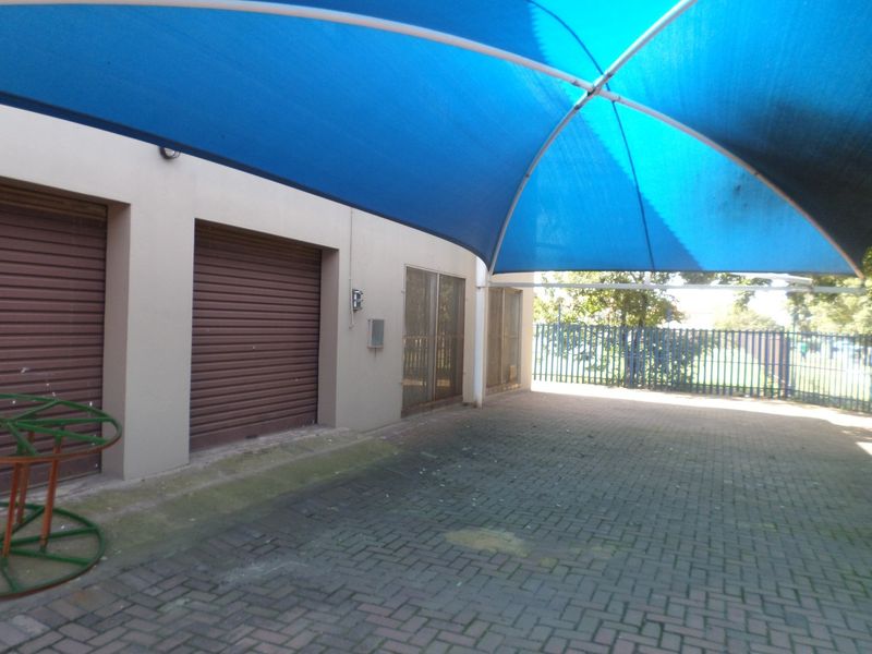 Rear exterior area featuring a large blue shade sail, paved ground, and multiple roller shutter doors providing secure access to the commercial building.
