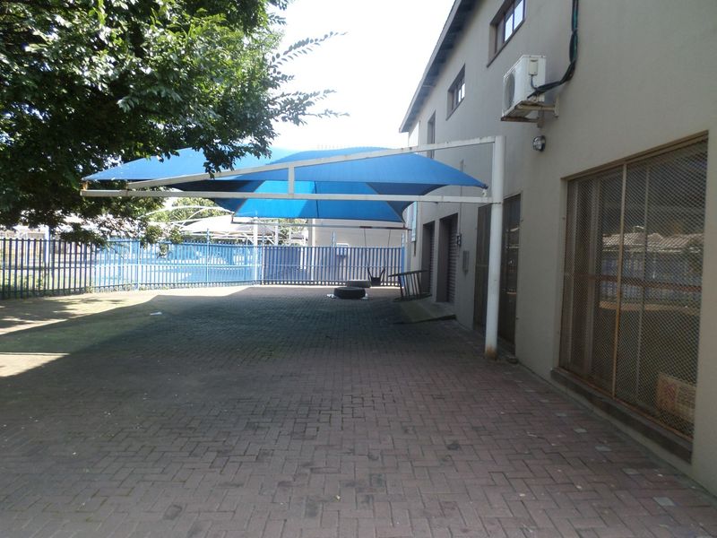 Rear exterior area featuring paved ground, a blue shade sail structure, security fencing, and an external air conditioning unit mounted on the building wall.