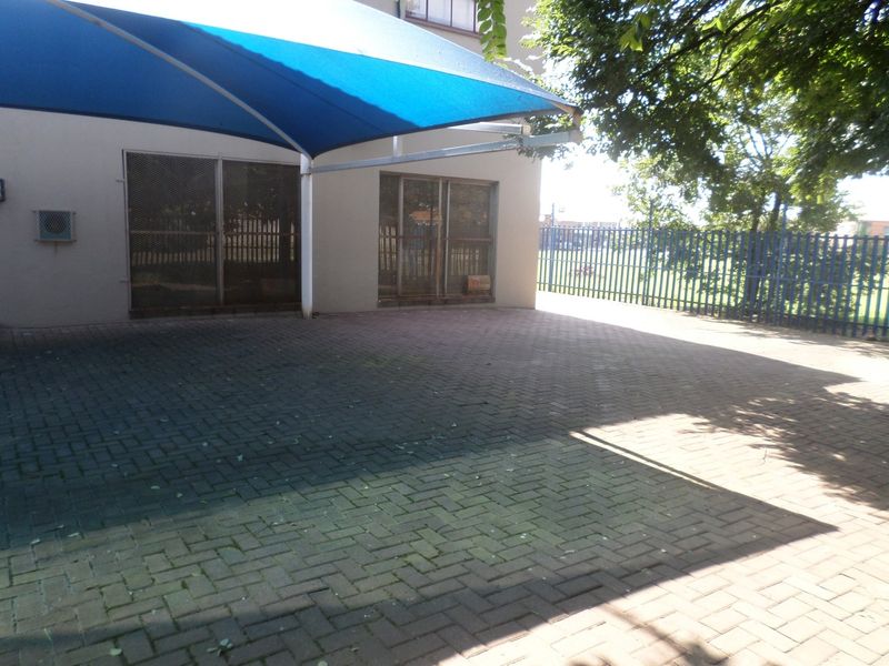 Rear exterior area featuring paved ground, a blue shade sail structure, security gates, and metal perimeter fencing.